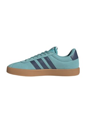 Zapatilla deportiva baja en verde azulado con rayas azul oscuro, lengüeta en el talón a juego, suela de goma marrón clara y cierre de cordones, vista lateral sobre fondo blanco.