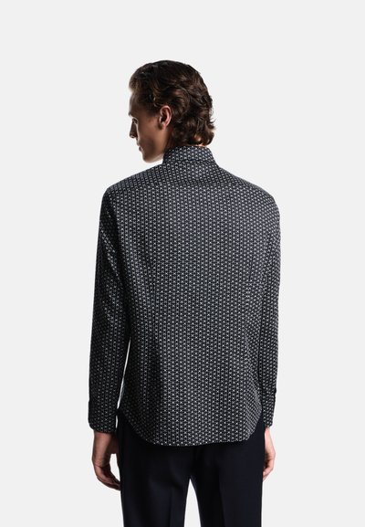 Camicia a righe bianche e nere con colletto alto, maniche lunghe e una vestibilità comoda, caratterizzata da un intricato design geometrico su tutta la superficie.