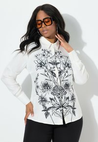 Blusa bianca con stampa floreale nera, maniche lunghe e colletto classico. Progettata con apertura a bottoni e tessuto liscio e leggero.