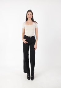 En mönstrad beige topp med fyrkantig halsringning, som är åtsittande, i kombination med höga svarta jeans. Svarta spetsiga ankelskor fulländar looken. Slät tygkvalitet och minimalistisk design.