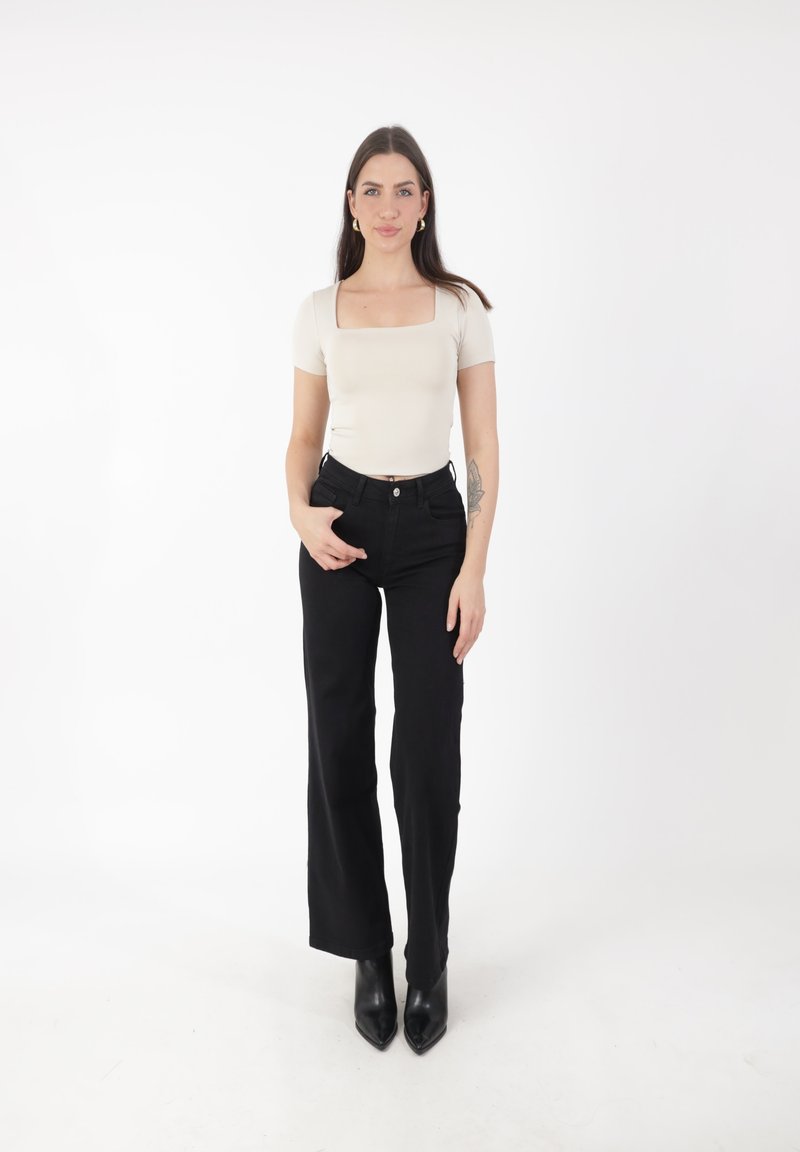 Top beige entallado de escote cuadrado, combinado con vaqueros negros de tiro alto. Botines negros de punta afilada completan el look. Tejido suave y diseño minimalista.