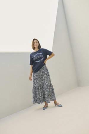 Marinblå T-shirt med vit text, kombinerad med en flödande, mönstrad maxi-kjol i svart och vitt. Blå spetsiga ballerinas kompletterar outfiten.