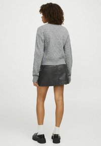 Maglione grigio a trecce con motivi a rombi, abbinato a una mini gonna nera in pelle e a scarpe nere chunky indossate con calzini bianchi.