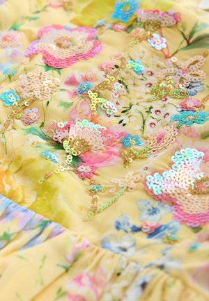 Material floral galben cu paiete irizate care formează forme de flori. Texturat cu detalii adunate, având accente de roz și albastru.