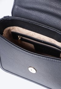Borsa a mano in pelle nera con un esterno strutturato, hardware dorato e rivestimento beige. Presenta una tasca interna con zip e slot per schede.