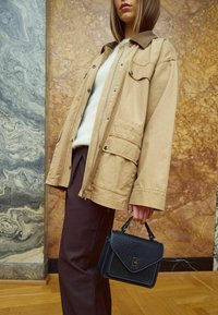 Béžová ľahká bunda s manžetovým golierom, so prednými vreckami. Skombinovaná s tmavohnedými nohavicami a textúrovanou čiernou kabelkou.