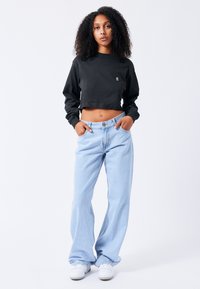 Black cropped sweatshirt and light blue wide-leg jeans, with a simple logo on the chest, paired with white sneakers. Soft fabric textures.