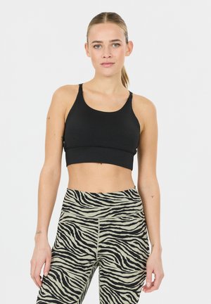 Ung kvinde med blondt hår sat op i hestehale iført en sort sports-bh og højtaljede leggings med zebra-print foran en ensfarvet baggrund.