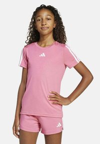 Camiseta atlética rosa de manga corta con rayas blancas, combinada con pantalones cortos a juego. Ambos presentan el logo de Adidas en blanco. Textura suave.
