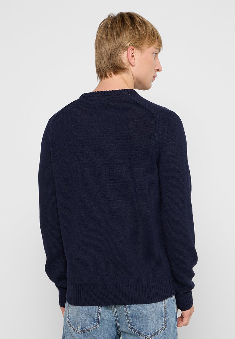 Pull en maille bleu marine à manches longues, col rond et finitions côtelées aux poignets et à l'ourlet. Présente un tissu texturé sans motifs visibles.