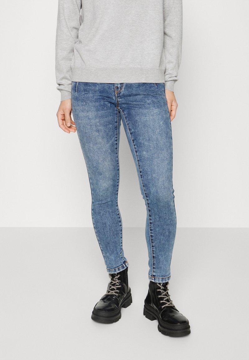 Jeans de ganga azul skinny com um acabamento desbotado, combinados com botas de combate pretas robustas com detalhes em prata e atacadores.