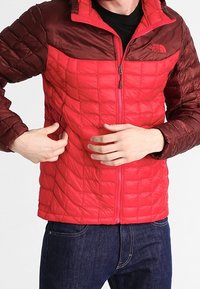 Giacca trapuntata rossa e bordeaux con zip frontale, caratterizzata da un colletto alto e un design a pannelli. Realizzata in materiale sintetico leggero e liscio.