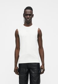 Witte katoenen mouwloze T-shirt met een subtiel logodetail, gecombineerd met zwarte leren cargobroek met meerdere zakken en een gladde textuur.