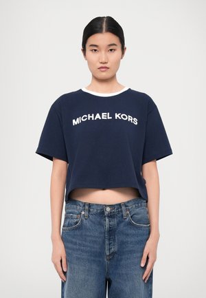 Navy sininen lyhyt t-paita, jossa on valkoinen "MICHAEL KORS" logo, lyhyet hihat ja pyöreä pääntie. Yhdistetty vaaleansiniset farkut.