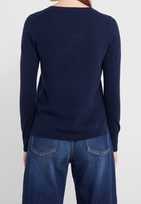 Pull bleu marine à manches longues en tricot doux, avec un col rond et une silhouette ajustée, associé à un jean large bleu clair.