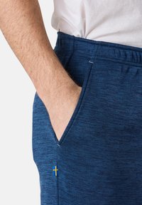 Marineblaue Sport-Jogginghosen aus weichem Stoff, mit einem Kordelzugbund, seitlichen Taschen und einem kleinen schwedischen Flaggenakzent in der Nähe der Tasche.