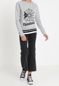 Szara bluza z czarną grafiką gwiazdy i napisem "Reebok". Prążkowane mankiety i dół w czerni i bieli. Połączona z czarnymi spodniami dzwonami i trampkami.