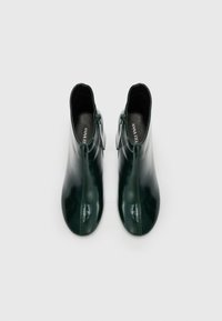 Bottines en cuir vert avec un design épuré, présentant une texture lisse, un bout rond et une fermeture éclair sur le côté pour faciliter l'enfilage.