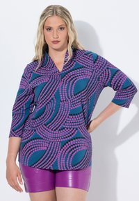 Bluse in Blau mit einem lebhaften violetten und schwarzen Kreisdesign, Dreiviertelärmel und leichtem V-Ausschnitt, kombiniert mit glänzenden lila Shorts.