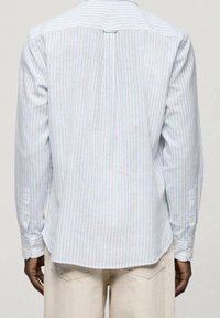 Jasnoniebieska koszula w paski z długimi rękawami, mankietami na guziki i detalem z plisą z tyłu. Wykonana z lekkiego, lekko teksturowanego materiału.