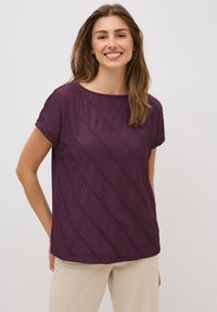 Purple short-sleeve top with wavy texture pattern and a round neckline, paired with light beige pants. Simple design, no visible hardware.
