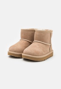 Botas de tobillo de ante beige con forro de pelo sintético, puntera redondeada y costuras decorativas. Cuentan con una suela de goma con un agarre texturizado.