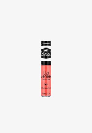 Kokie Professional Lip Veneer Cream -huulikiilto korallinpunaisessa sävyssä, musta-valkoraidallinen korkki, 6 ml puteli.