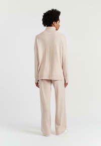 Pull en maille rose clair avec col montant, coupe décontractée et manches longues, assorti à un pantalon large rose clair.