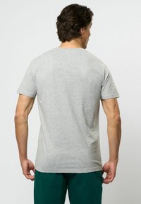 Grå t-shirt med kort ärm i bomullsblandning, med klassisk rundhals och slät yta. Bärs med mörkgröna byxor.