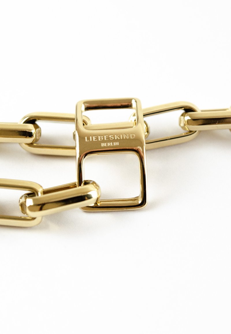Gouden schakelarmband met verlengde schakels en een vierkante sluiting, gegraveerd met "LIEBESKIND BERLIN." Glad, glanzend metaalafwerking.