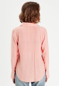Chemise à manches longues en corail clair avec des rayures verticales blanches. Caractéristiques : col pointu, poignets à bouton et ourlet incurvé. Texture douce.