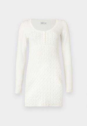 Bijela pletena haljina dugih rukava s uzorkom kabelskog pletenja, okruglim izrezom i kopčanjem na gumbe na jednobojnoj pozadini.