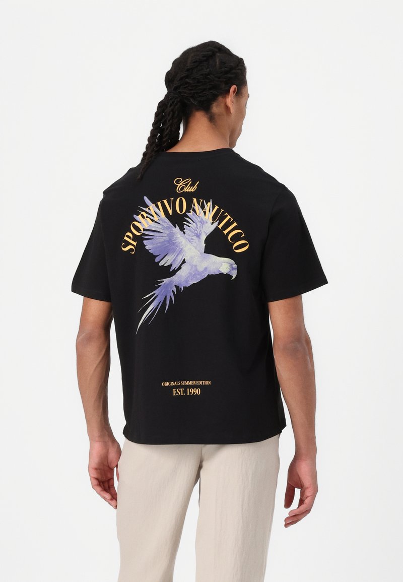 Camiseta negra con un gráfico colorido de loro en la parte posterior, con texto en dorado. Corte regular y mangas cortas. Material ligero de algodón.