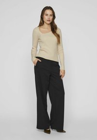 Top beige a maniche lunghe a coste con scollatura quadrata abbinato a pantaloni neri a gamba larga. Il top è aderente mentre i pantaloni sono larghi e fluidi.