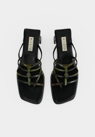Μαύρα σανδάλια με τετράγωνη μύτη και τακούνι, με λεπτά σκουροπράσινα λουράκια και μικρό αγκράφα, με ετικέτα "MIISTA" στην εσωτερική σόλα.