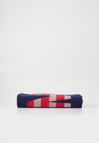 Serviette multicolore avec une base bleue et des motifs en diagonale rouges et blancs, soigneusement enroulée avec une texture et une finition visibles.