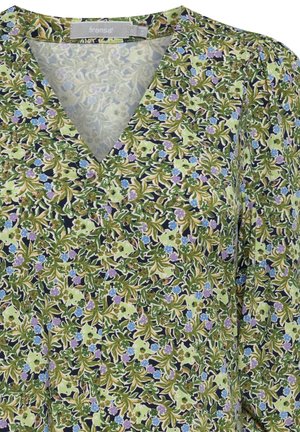 Blommig blus i grönt, blått och lila med v-ringning. Har ett texturerat mönster av blad och blommor på en mörk bakgrund.