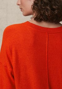 Heller orange, übergroßer Pullover mit einem gerippten Halsausschnitt, strukturiertem Strickstoff und einer mittigen Nahtdetails auf der Rückseite.