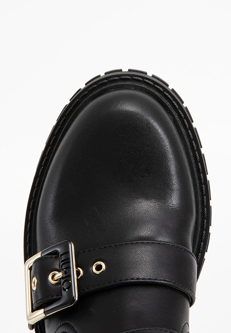 Schwarzer Lederschuh mit runder Spitze, strukturiertem Obermaterial, verstellbarem Schnallenriemen und goldenen Akzenten. Dicke Gummisohle mit profilierter Oberfläche.