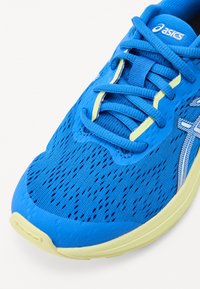 Chaussure de sport bleue avec une tige texturée, présentant des accents et des lacets jaunes, et une semelle en caoutchouc de couleur claire. Logo Asics visible.