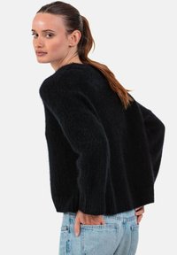 Schwarzer, flauschiger Strickpullover mit rundem Ausschnitt und weiten Ärmeln, kombiniert mit hellblauen Jeans. Strukturiertes, kuscheliges Design.