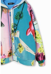 Färgglad hujacka med en blandning av blommönster och abstrakta mönster, tillverkad av mjukt tyg med dragkedja framtill och två sidofickor.