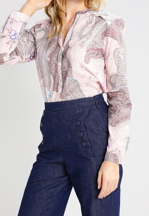 Roze blouse met paisley-patroon, een kraag met knopen en lange mouwen, gecombineerd met een donkerblauwe denim broek met hoge taille en knopen aan de zijkant.