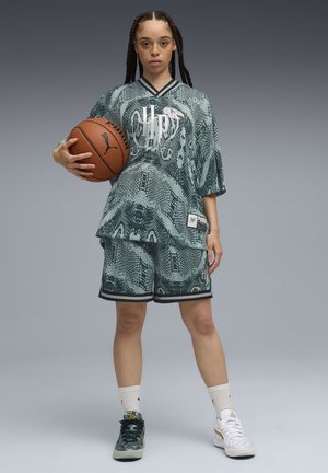 Green patterned oversized jersey with snake design, paired with matching shorts. Player holds a brown basketball, wearing black and white sneakers.