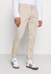 Béžové bavlněné chinos s rovnou nohavicí, s knoflíkovým zapínáním a ohrnutými manžetami, doplněné bílými sportovními botami.