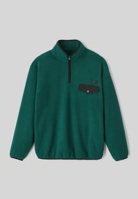 Pull verde en polaire avec un col zippé demi-hauteur. Il présente une poche poitrine noire avec un bouton pression et des poignets élastiques. Texture douce, design décontracté.