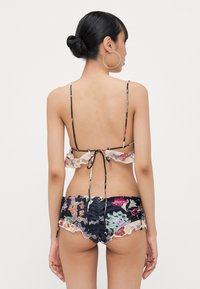 Blomstrende to-dels badedrakt med svart bakgrunn, volangdetaljer på toppen og matchende shorts, med livlige flerfargede mønstre.