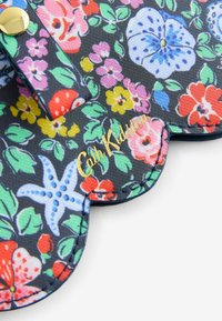 Stoff mit Blumenmuster auf schwarzem Hintergrund, der bunte Blumen und Blätter zeigt. Goldenes Logo "Cath Kidston" nahe der gewellten Kante.