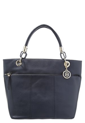 Schwarze Leder-Shopper-Tasche mit goldener Hardware, Außenreißverschlussfach, doppelten Griffen und rundem goldenen Anhänger mit Initialen, der auf der rechten Seite hängt.