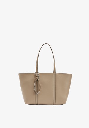 Beżowa skórzana torba typu tote z dwoma uchwytami oraz ozdobnym węzłem i łańcuszkiem na środku przedniej strony.